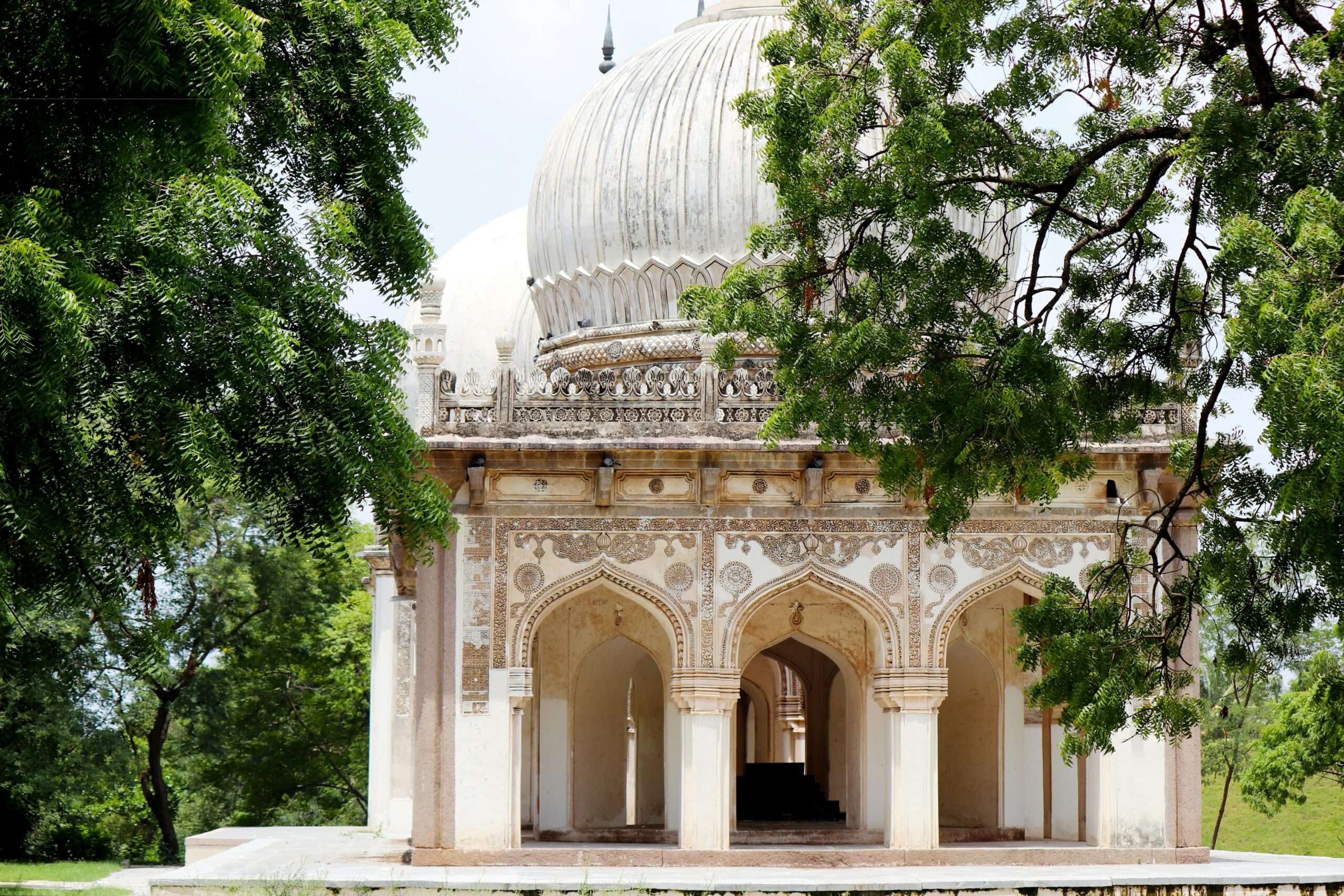Intricate architecture of the Qutb Shahi Tombs in Hyderabad, surrounded by lush greenery.
